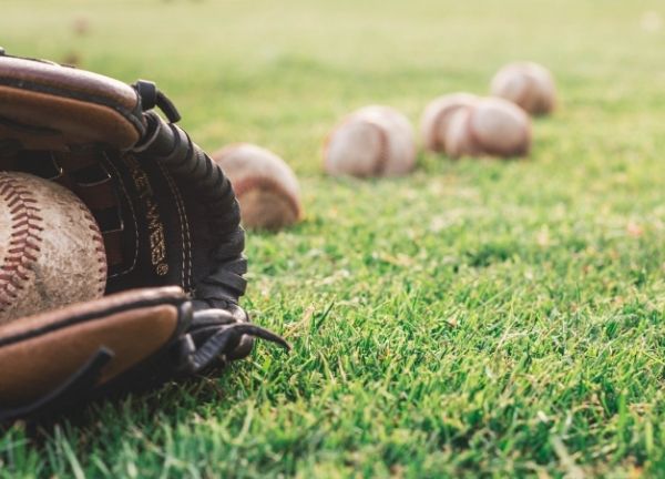 A row of baseballs on the ground with one in a glove.